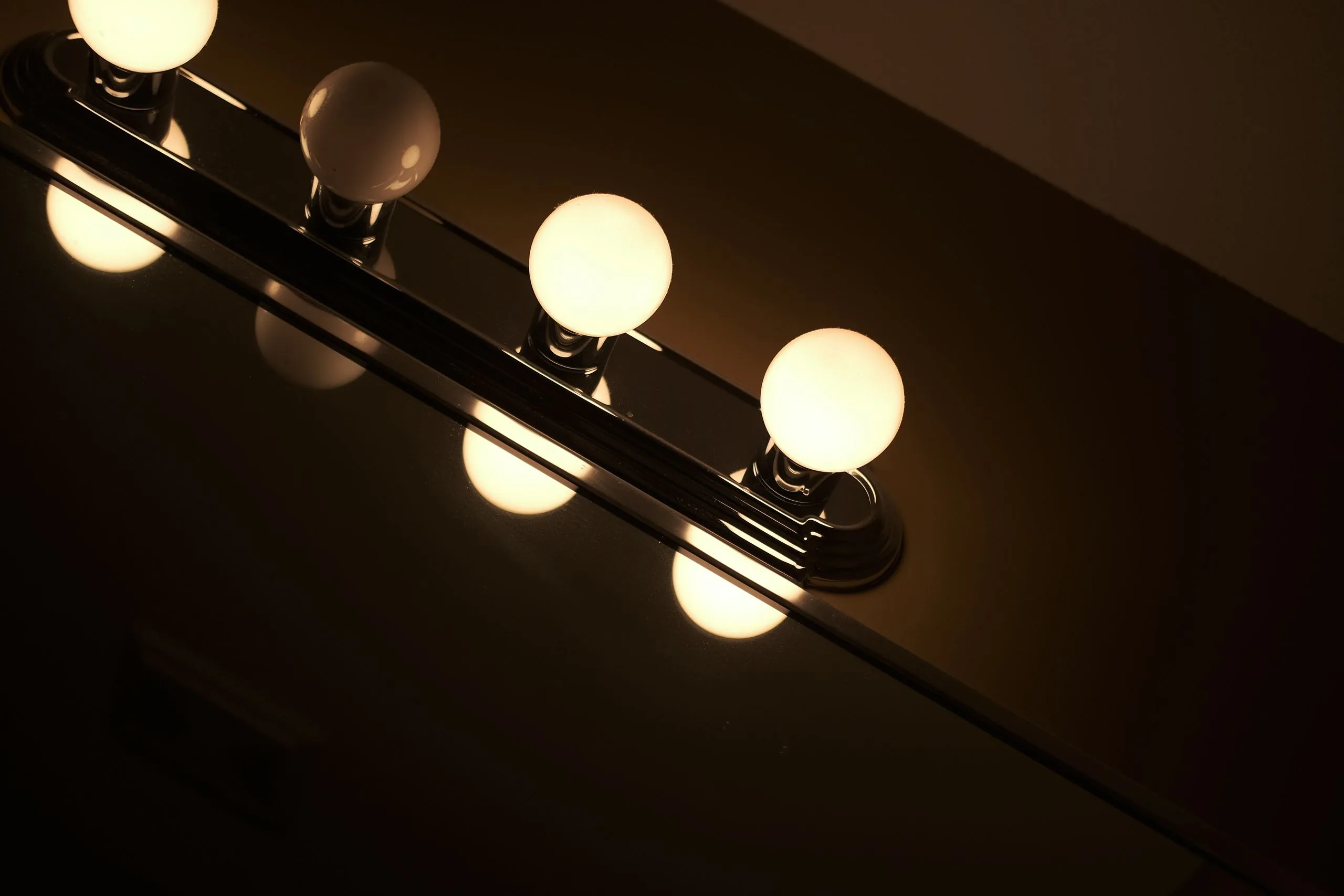 Salle de bain moderne éclairée par un luminaire mural au-dessus du miroir, ambiance douce et carrelage clair.