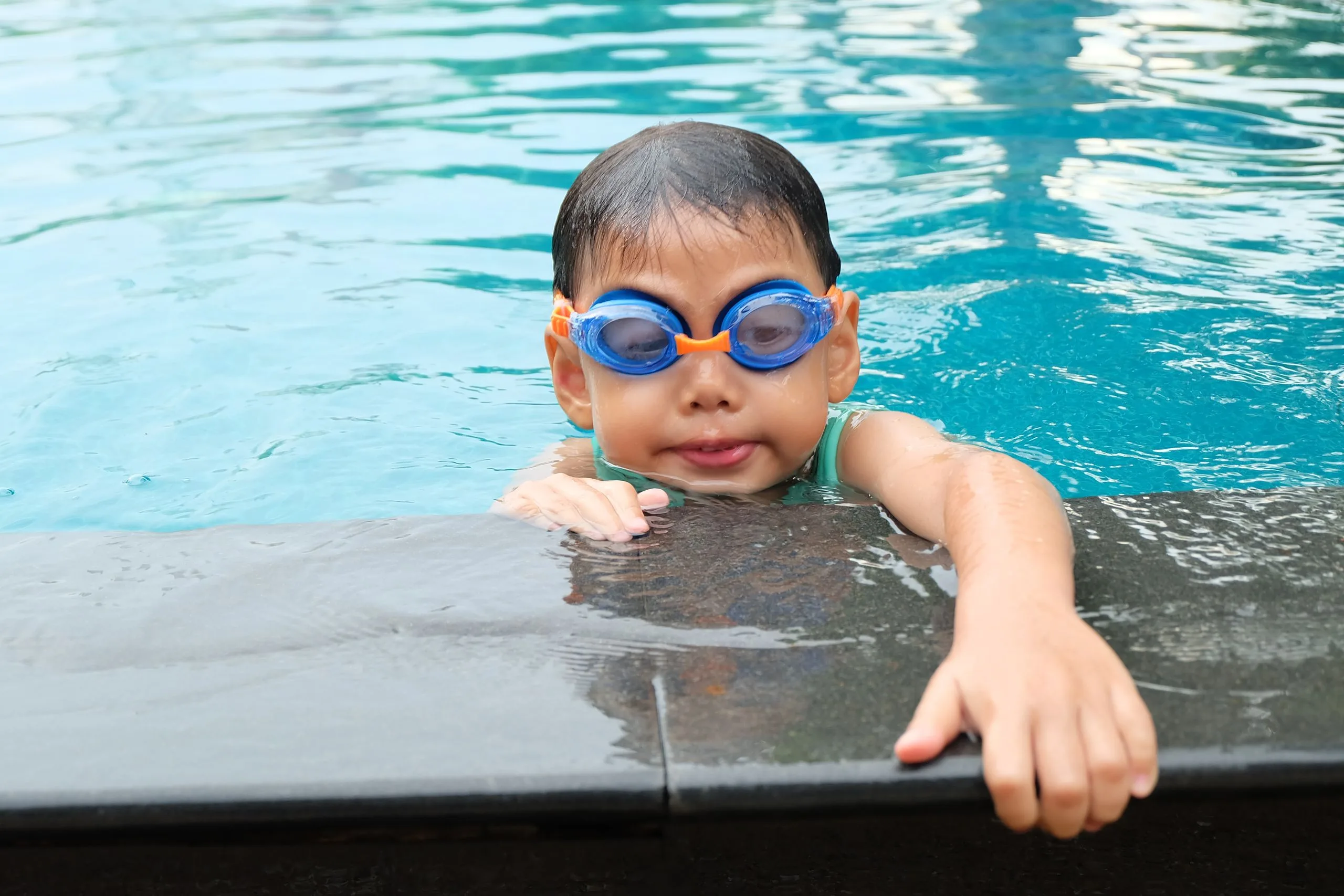 Jeune enfant souriant dans une petite piscine gonflable colorée installée dans un jardin ensoleillé